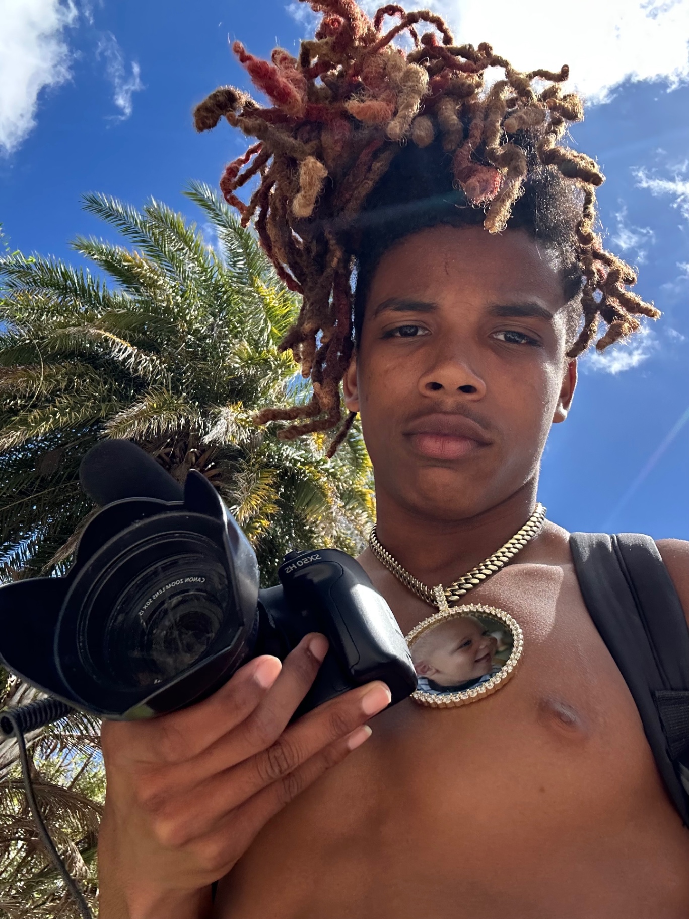 Red holding a Canon camera under a palm tree